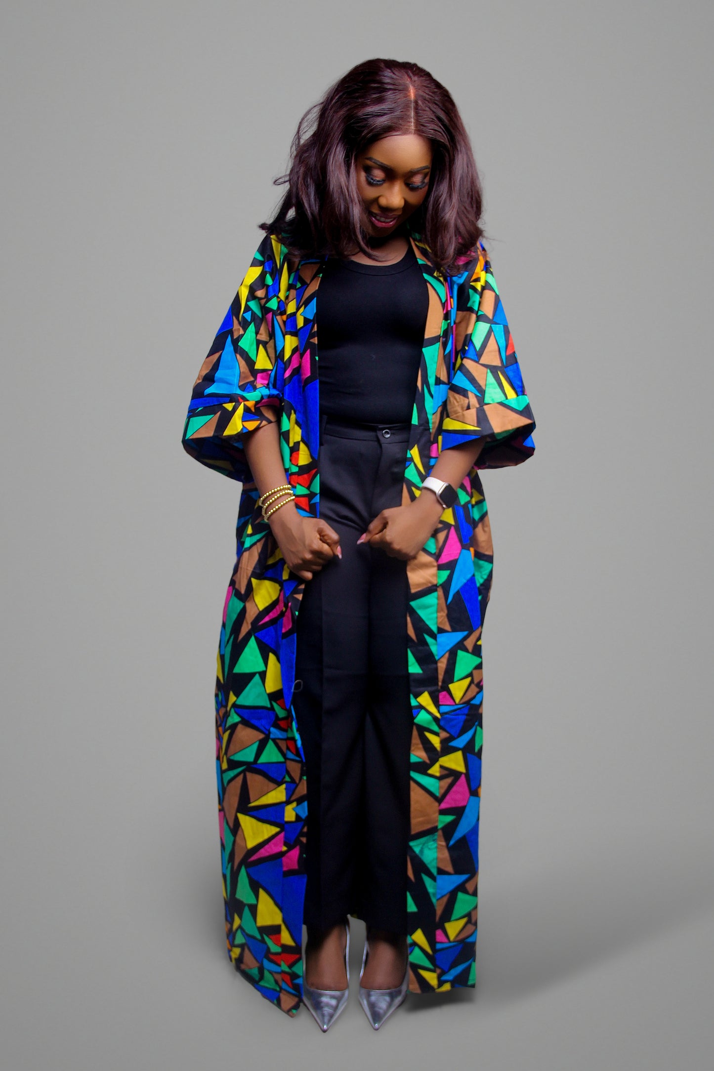 A person wearing a longline kimono jacket with a colorful geometric pattern over a black tank top and trousers.