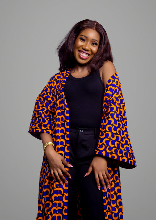 A person wearing a longline kimono jacket with a vibrant orange and blue crescent pattern over a black tank top and trousers.