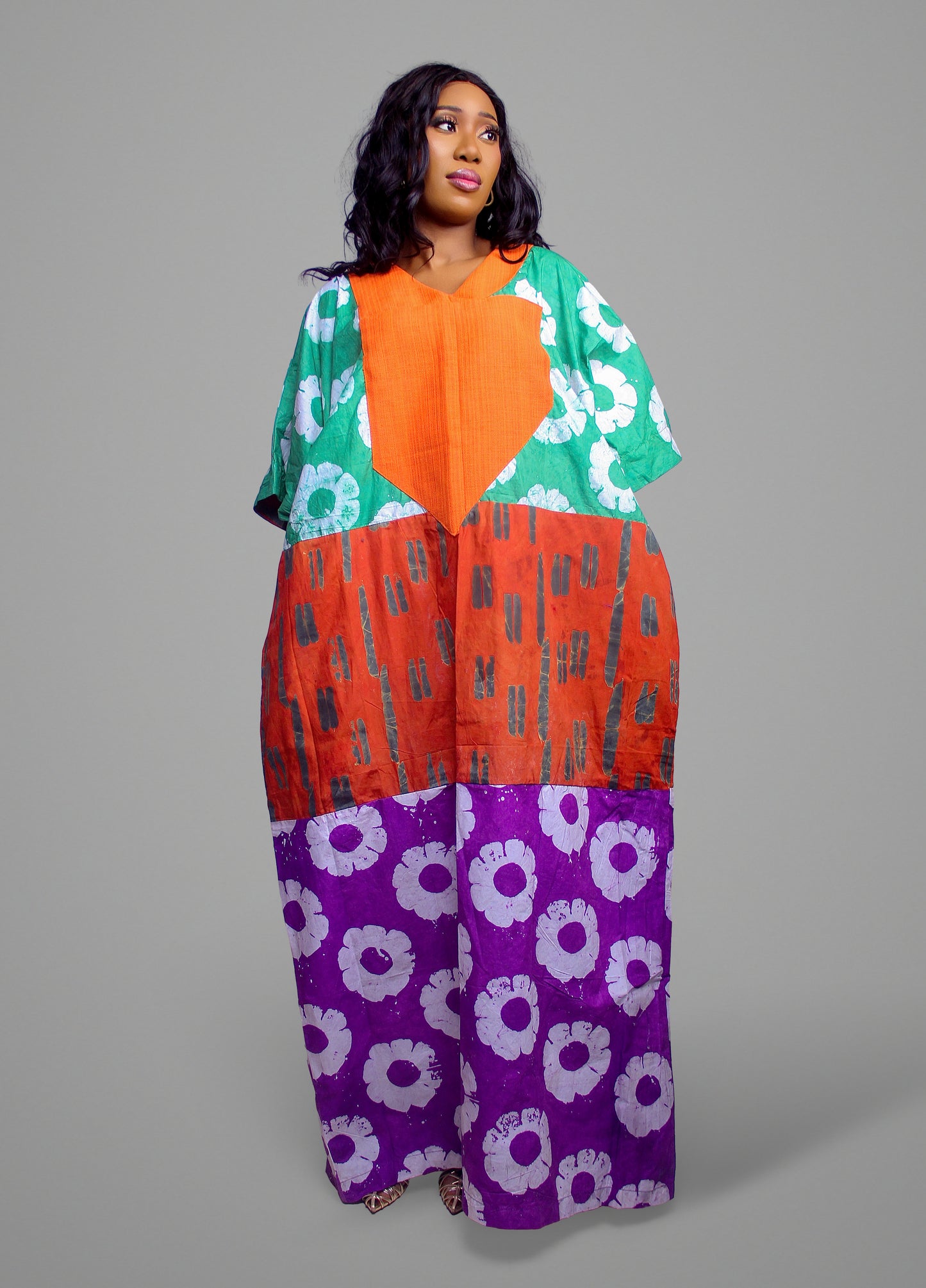 Kaftan dress with an orange chest panel and stacked sections of floral, striped, and heart motifs in green, orange, and purple.