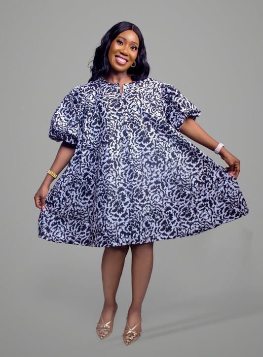 A woman wearing a black and white floral damask dress with dramatic puff sleeves and a flared skirt
