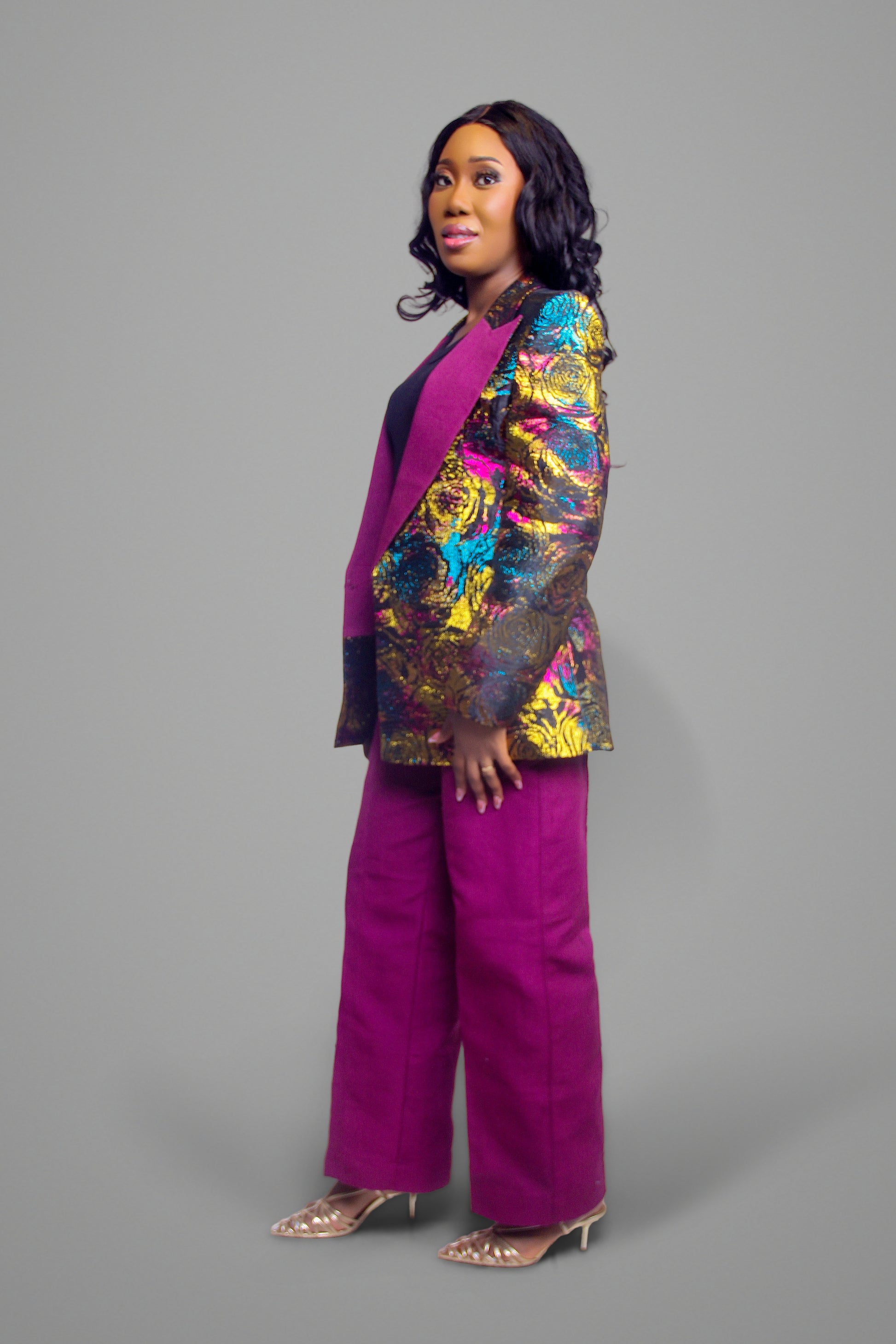 Side profile of a metallic floral brocade blazer in gold, blue, and magenta paired with magenta wide-leg trousers.