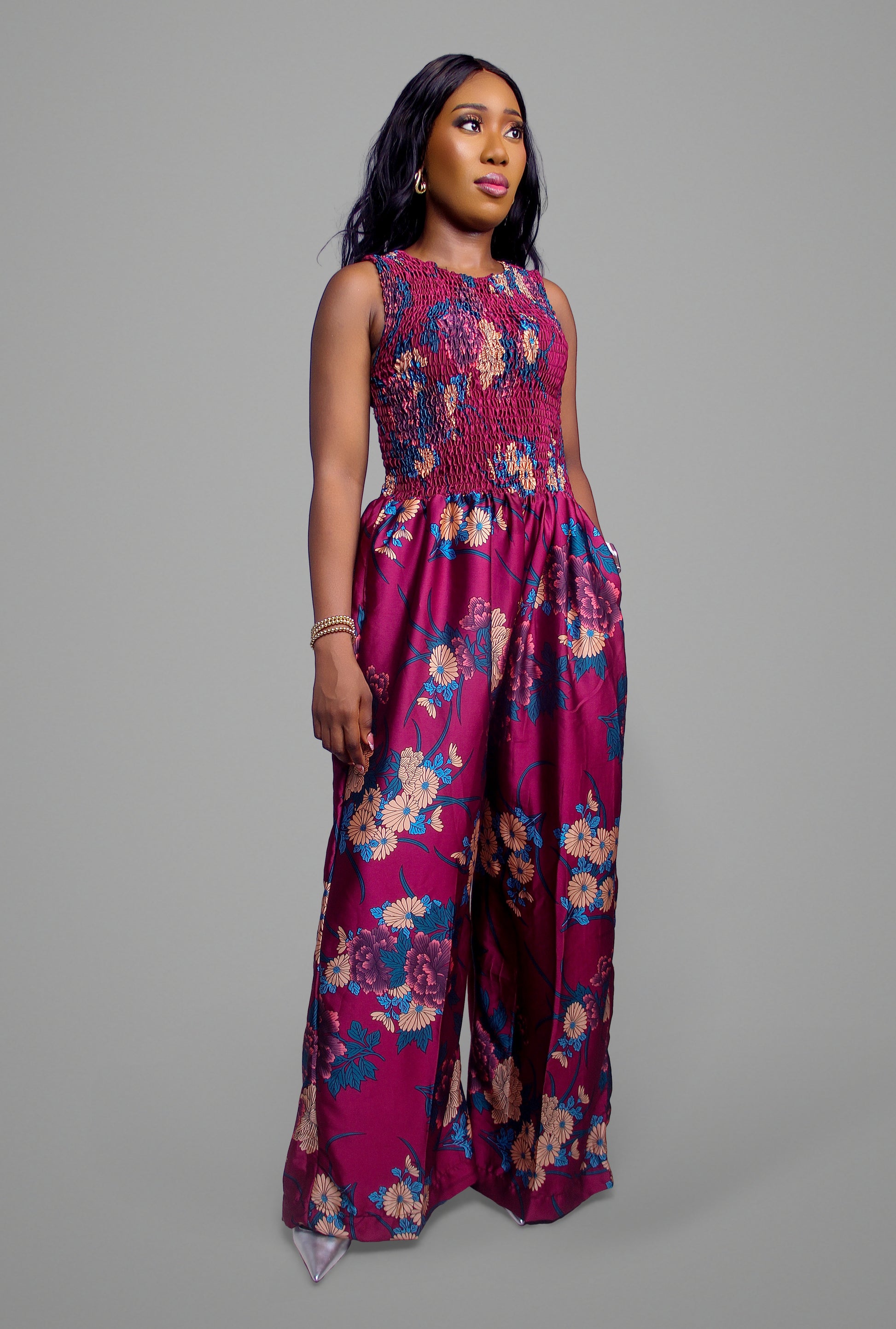 A full-body view of a deep red floral print jumpsuit with a smocked bodice and wide legs.
