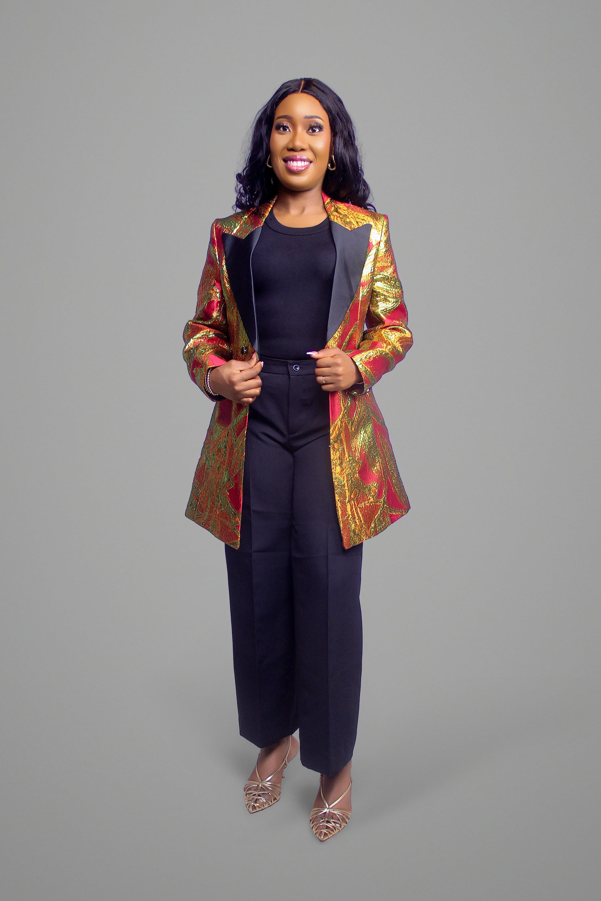 Full body view of woman wearing a cropped gold and red floral brocade blazer with black lapels