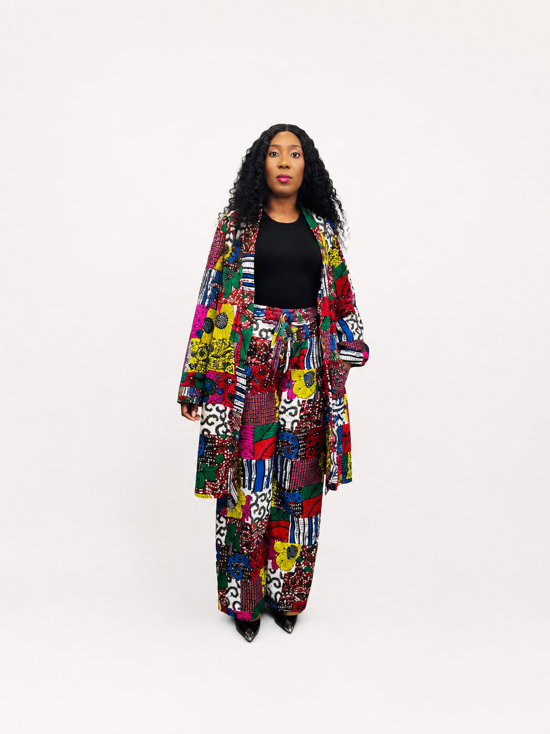 Full view of a woman wearing a vibrant multi-patterned patchwork African print duster coat and matching wide-leg trousers
