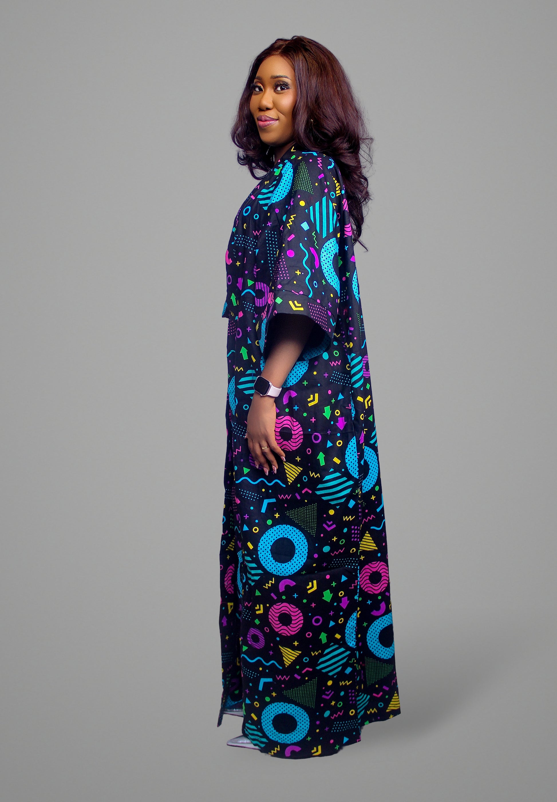 A side view of a floor-length maxi kaftan featuring a bold black, blue, pink, and yellow Memphis-style geometric print on 100% cotton fabric.