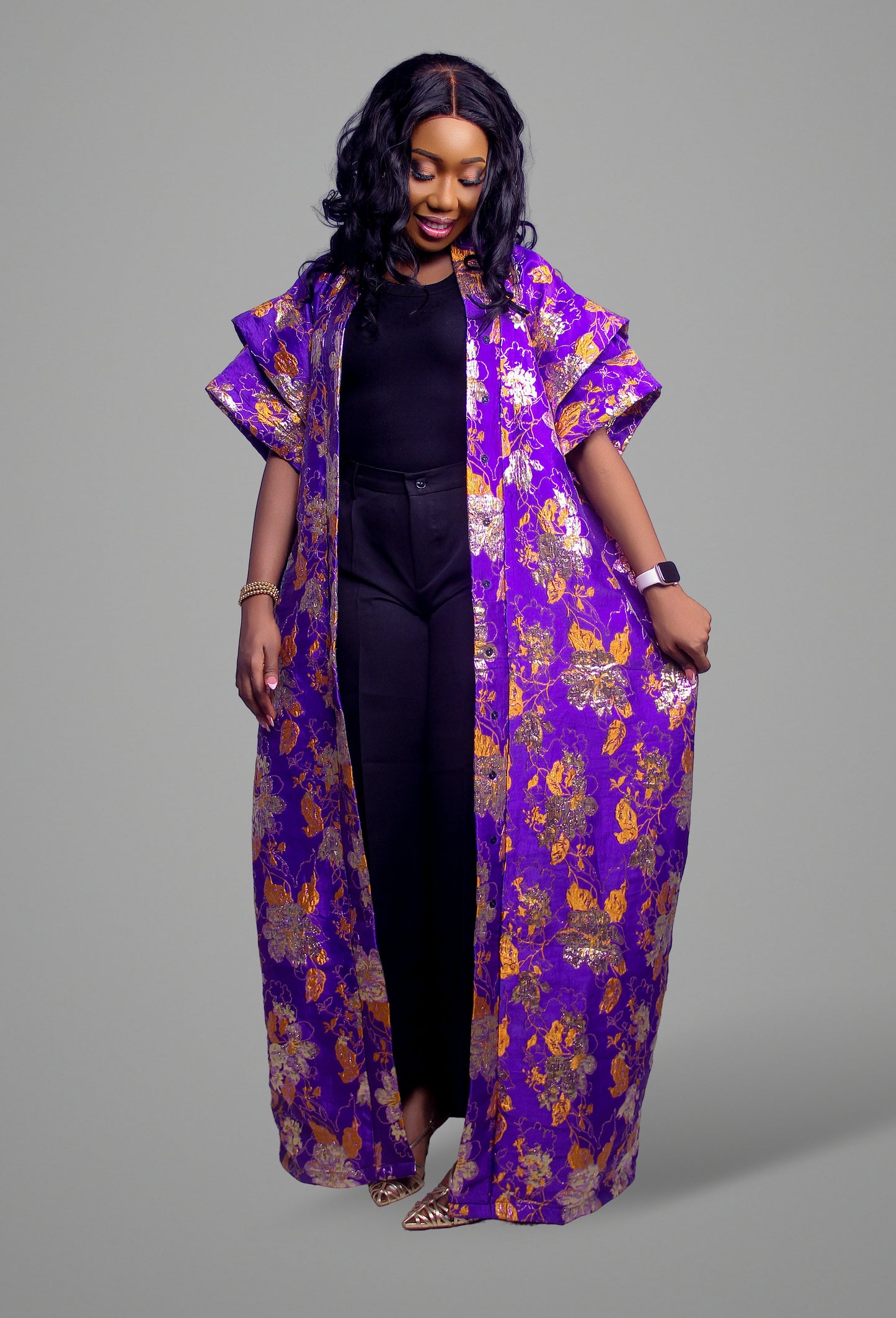 Purple duster coat in floral brocade fabric with metallic gold accents worn over a black top and trousers