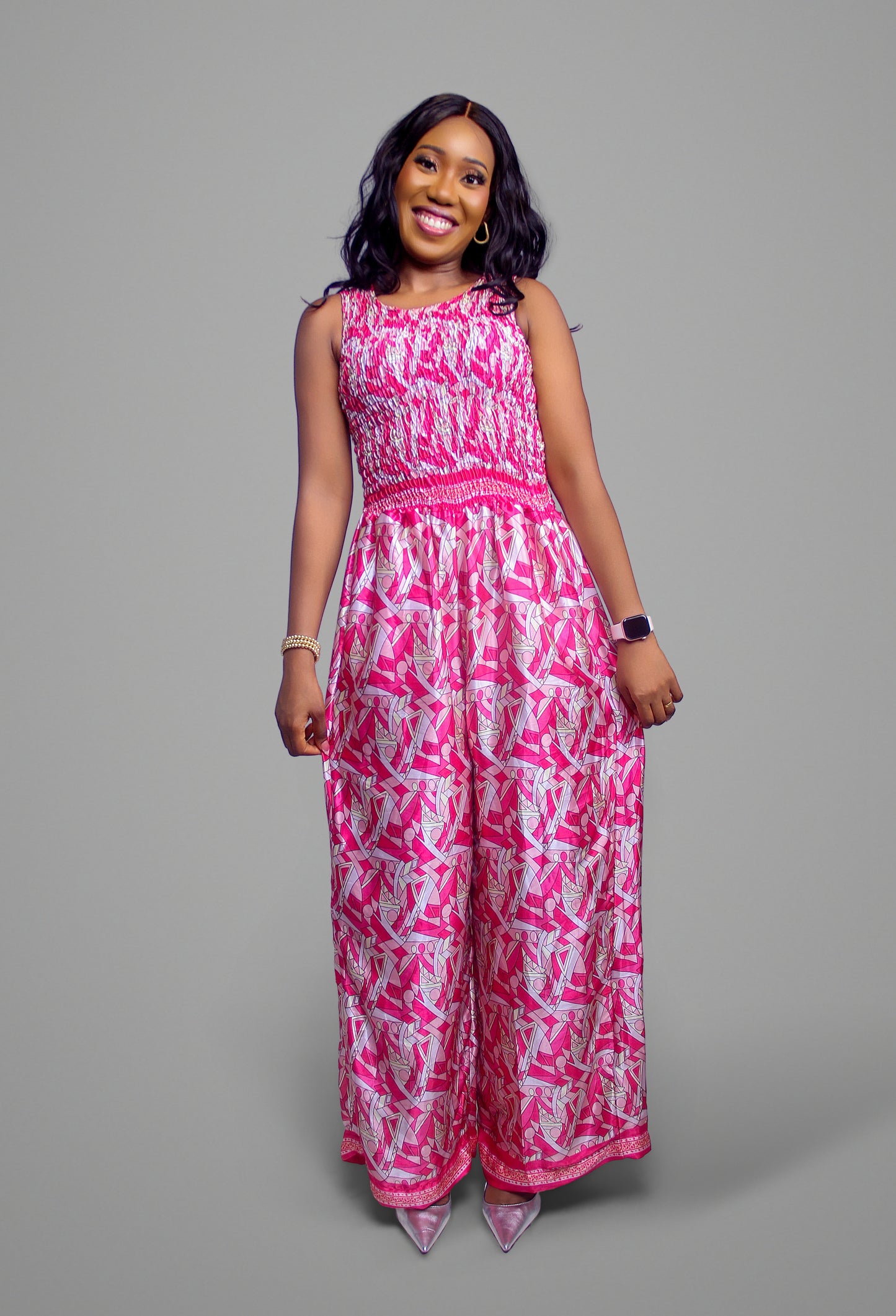 A full-body view of a vibrant pink geometric print jumpsuit with a smocked bodice and wide legs.