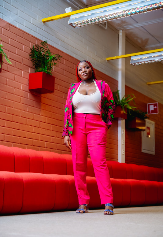 Full-length shot of a woman modeling a bright pink trouser suit with patterned blazer accents.
