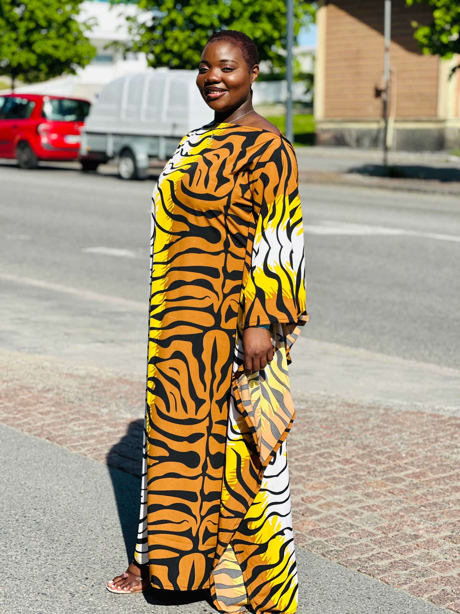 Side profile of a woman outdoors wearing a flowing orange, yellow, and black tiger-print kaftan.