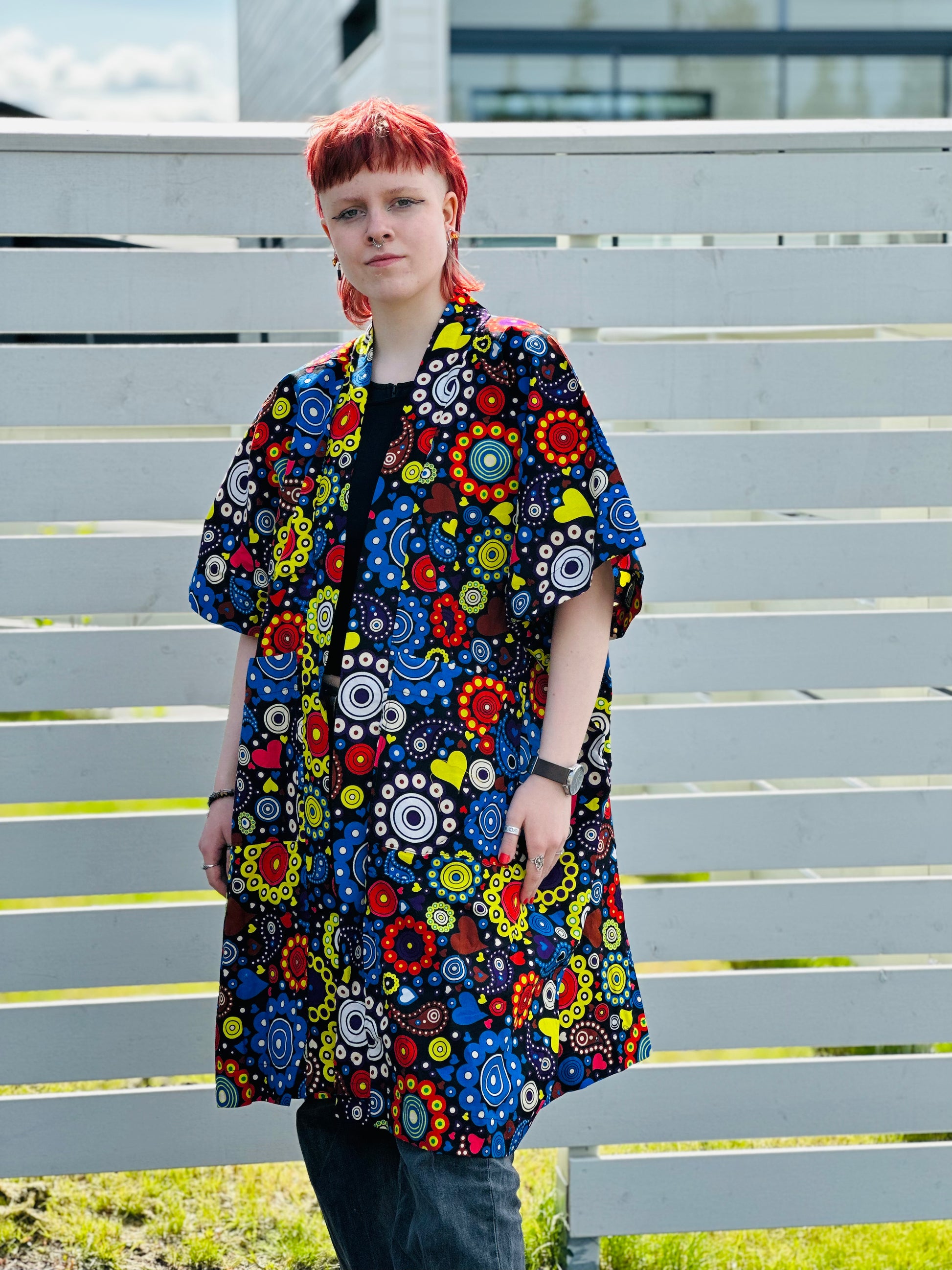 Red-haired model posing in a vibrant, multi-colored floral patterned kimono over dark clothing outdoors.