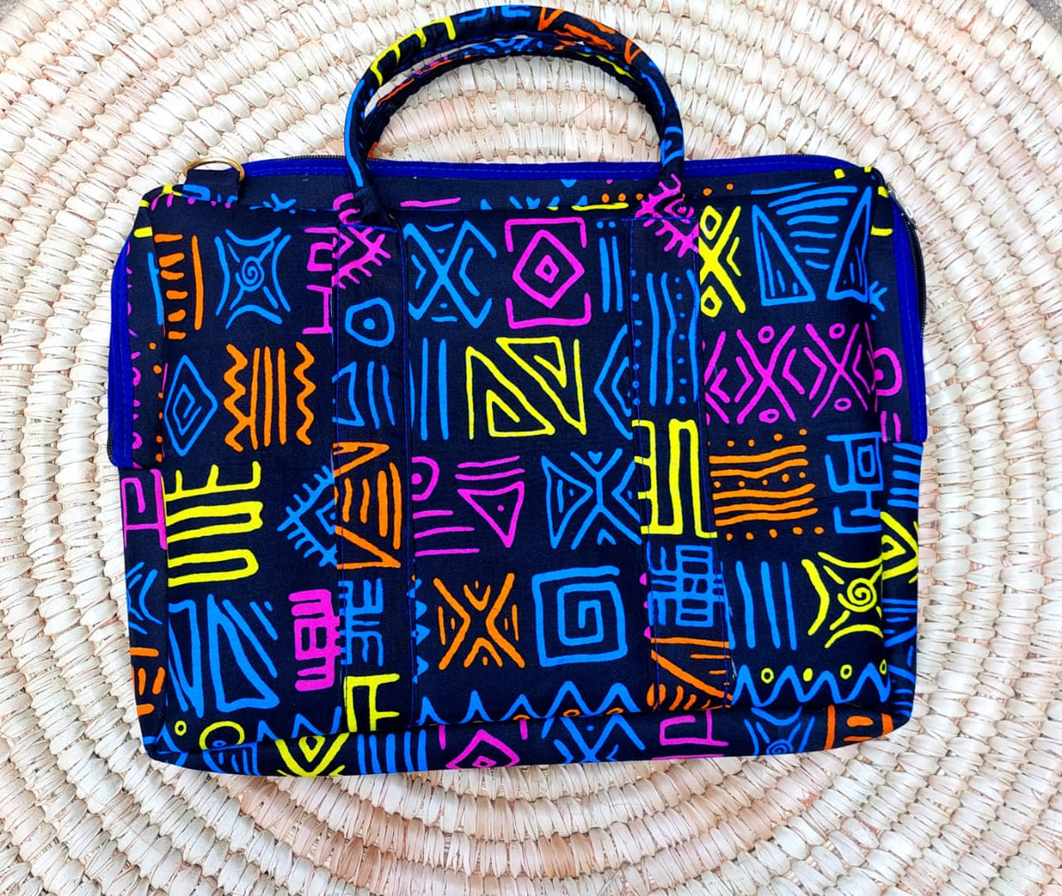 Black fabric laptop bag with neon tribal symbols resting on a circular woven straw mat.