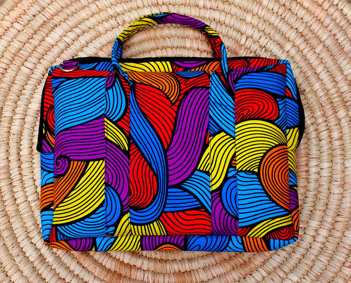 Colorful laptop bag with wavy abstract patterns in bright colors on a woven straw mat.